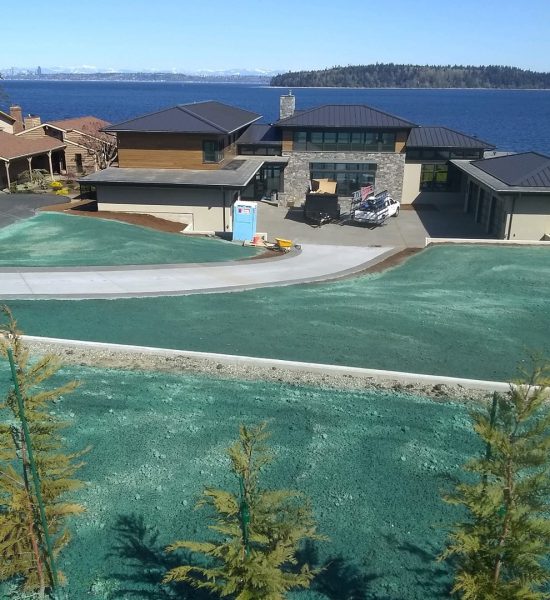 A modern house overlooks a body of water, with green hydroseeded lawns and a driveway in front.