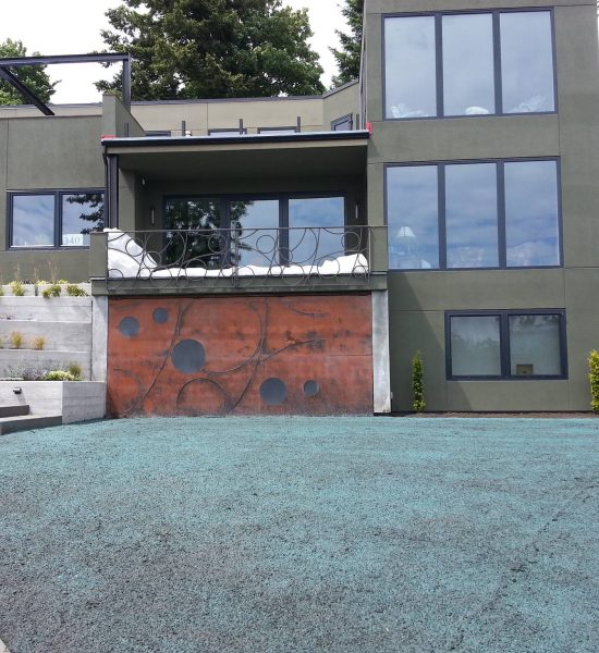 Modern two-story house with large windows, abstract garage door, and freshly seeded blue-green front yard.